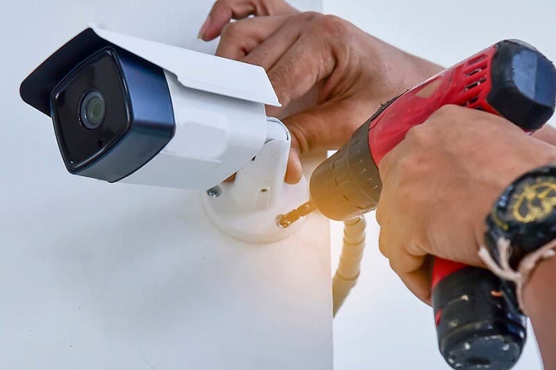 Hands using a drill to mount an outdoor CCTV camera