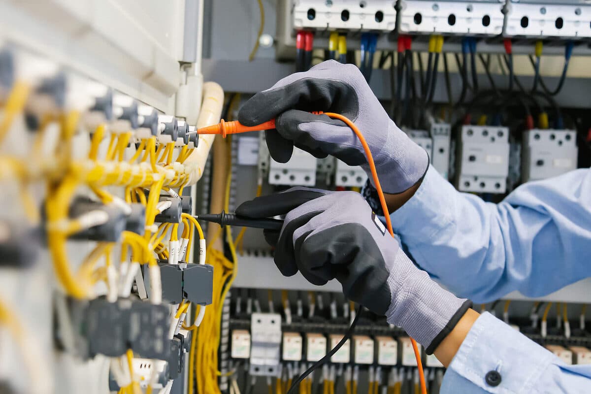Gloved hands testing wiring inside an electrical control panel