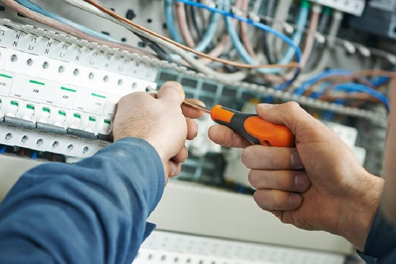 Hands fastening wiring beside circuit breakers in a control panel