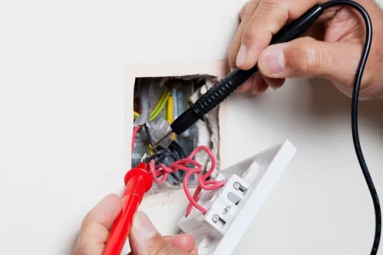 Hands testing electrical wiring inside a wall fitting