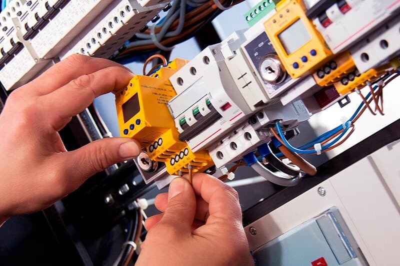 Hands adjusting a timer beside circuit breakers in a switchboard