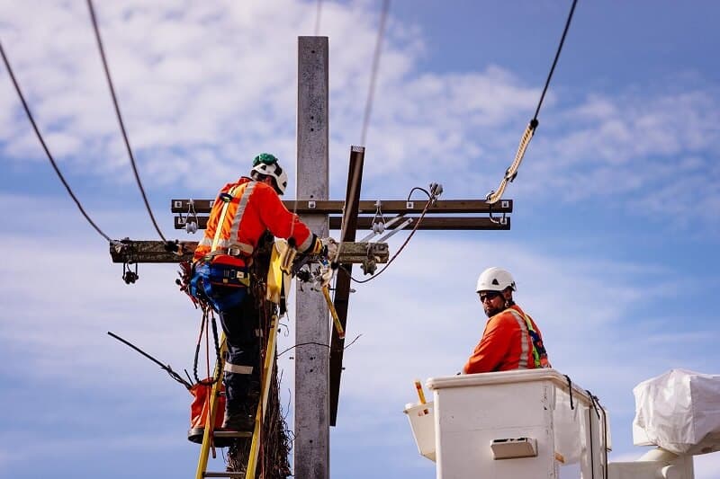 Two workers in safety equipment carrying out work on a power pole