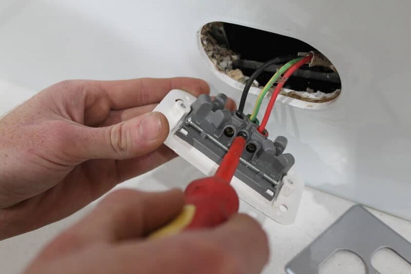 Hands wiring a wall-mounted electrical outlet