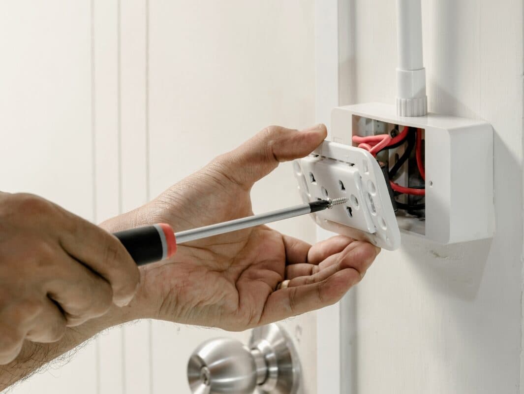 Hands connecting electrical wiring inside a wall fitting