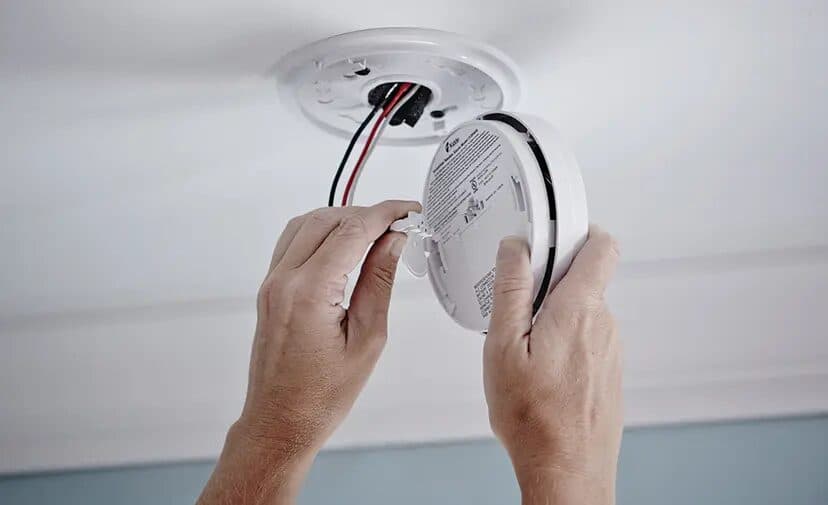 Hands fitting a smoke alarm to a ceiling