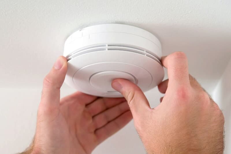 Hands fitting a smoke alarm to a ceiling